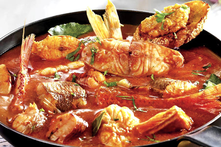 Fish stew in a pan with red sauce and herbs