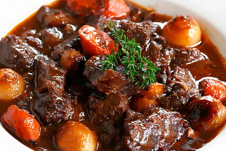 Beef bourguignon with carrots and onions on a white plate