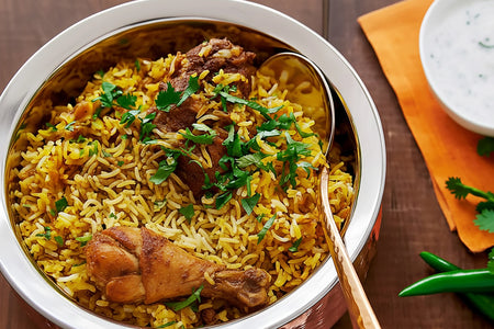 Biryani dish with chicken and rice in a metal bowl on a wooden table.