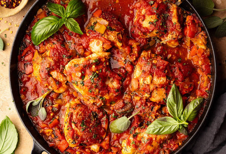 Skillet with tomato-based chicken dish garnished with basil leaves