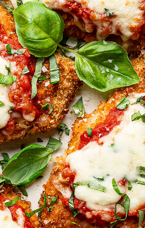 Close-up of breaded chicken with tomato sauce and cheese, garnished with basil leaves.