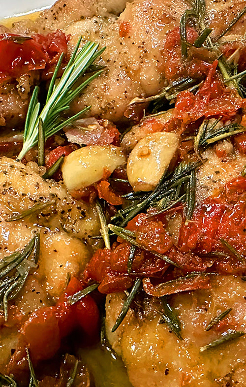 Close-up of roasted chicken with tomatoes and herbs on a plate