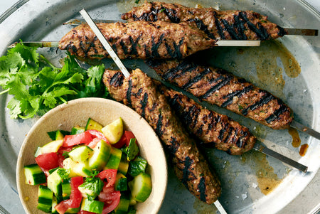 Grilled skewers of meat with a side of salad on a metal plate.