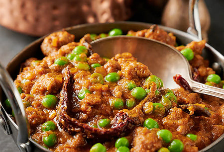 Carnival-style chicken with green peas in a metal dish with a spoon.