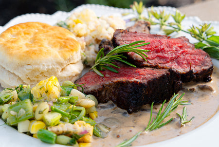 Plated dish with sliced beef, biscuit, and vegetable salad on a white plate.