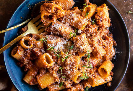 Pasta dish with sauce and herbs in a blue bowl with a gold fork.
