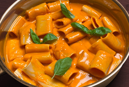Pasta dish with orange sauce and basil leaves in a metal pan