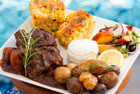 Plated dish with meat, potatoes, corn, and salad on a blurred outdoor background
