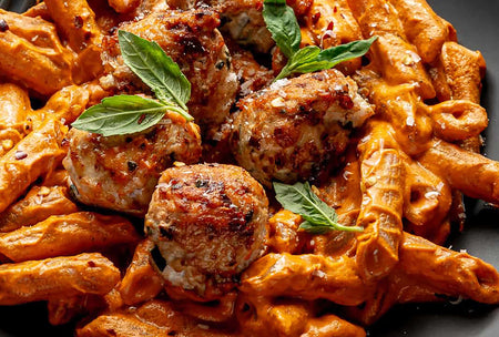 Pasta with meatballs and fresh basil leaves on a dark surface