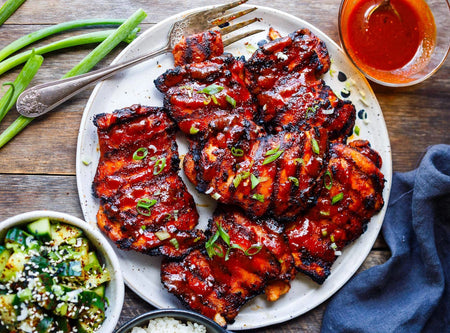 Platter of grilled chicken wings with a side of green vegetables on a wooden table.