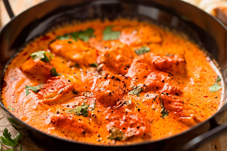Chicken dish in a rich orange sauce with herbs in a black skillet.